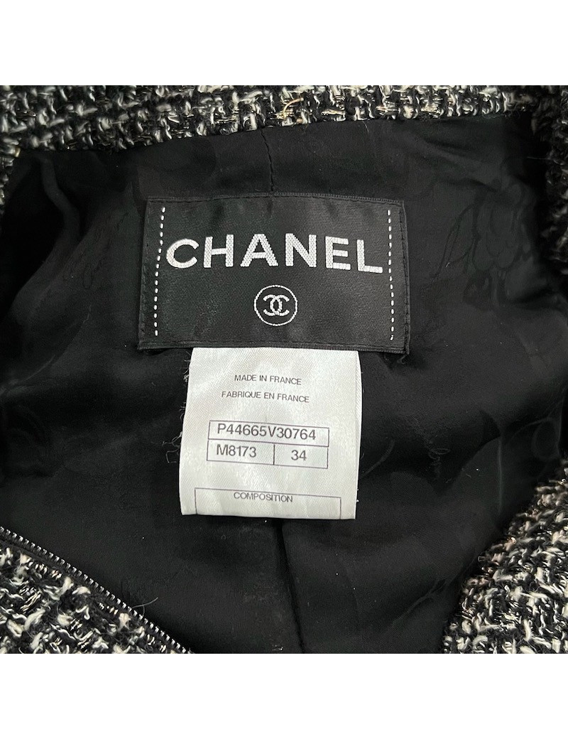 Veste T34 CHANEL en tweed noir et blanc avec fil doré. Fermeture avec zip et deux poches passepoilées sur le devant